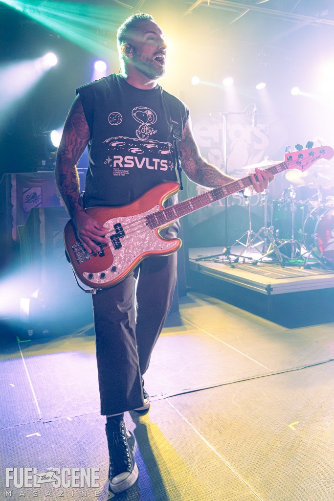 A musician passionately playing a bass guitar on stage during a performance, illuminated by vibrant stage lights.
