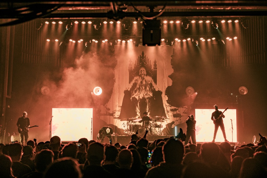 A live performance by Fit For a King at The Tabernacle, featuring dynamic stage lighting and a dramatic backdrop, with the band engaging the enthusiastic audience.