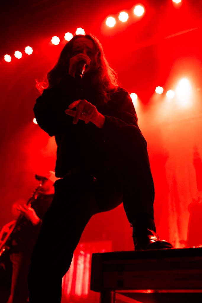 A singer with long hair performs on stage, illuminated by red lights, capturing the energy of a metalcore concert.