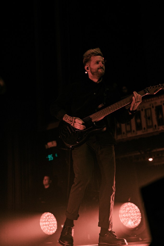 A guitarist performing passionately on stage during a metalcore concert, with dramatic lighting effects and a focused expression.