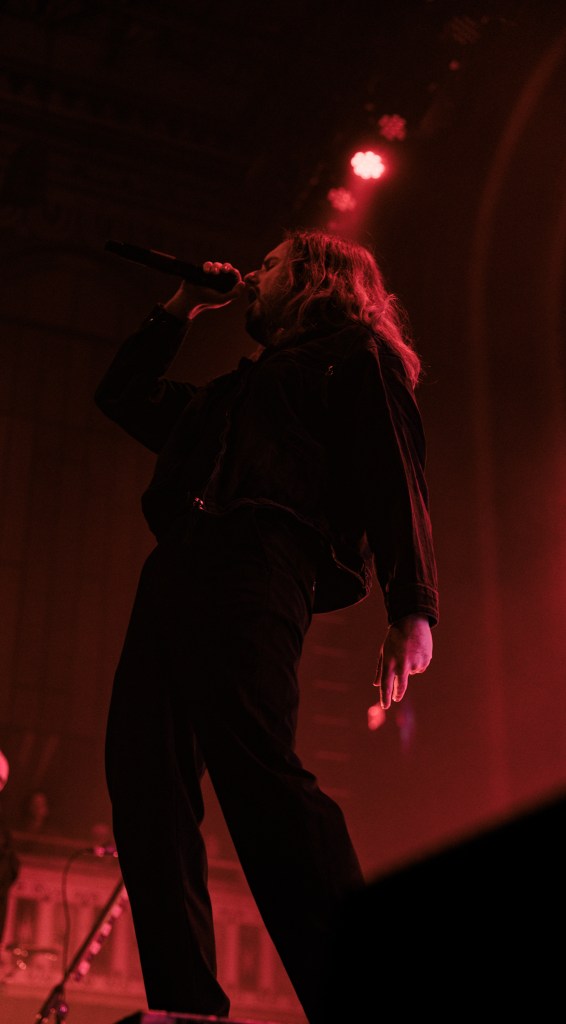 A singer performing on stage with a microphone in hand, highlighted by dramatic lighting, creating an intense atmosphere.