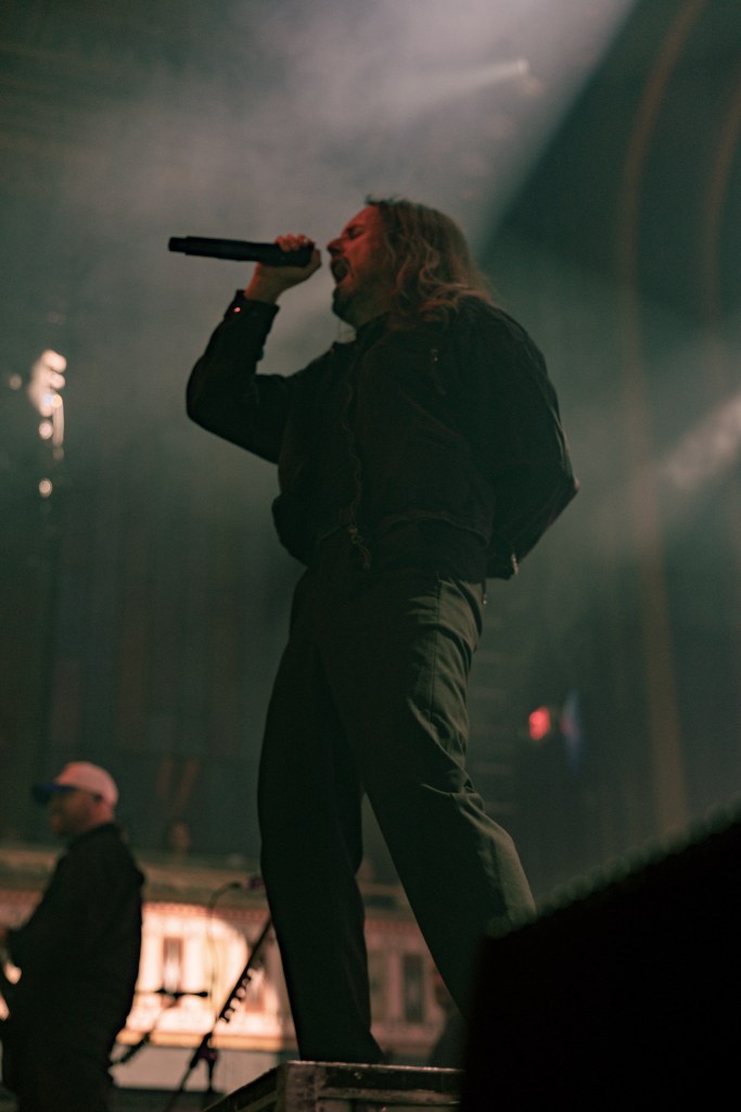 A vocalist passionately performing on stage with a microphone, surrounded by dramatic lighting and a hazy atmosphere.