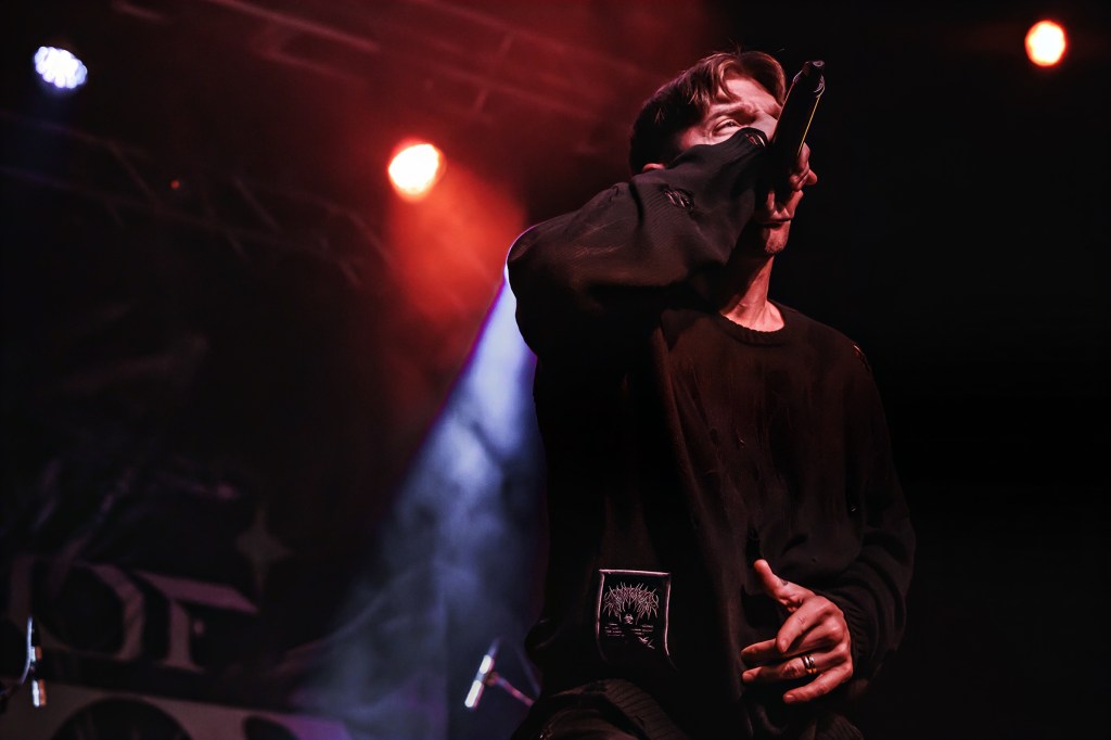 A singer performing on stage, holding a microphone, with dramatic stage lighting in the background.